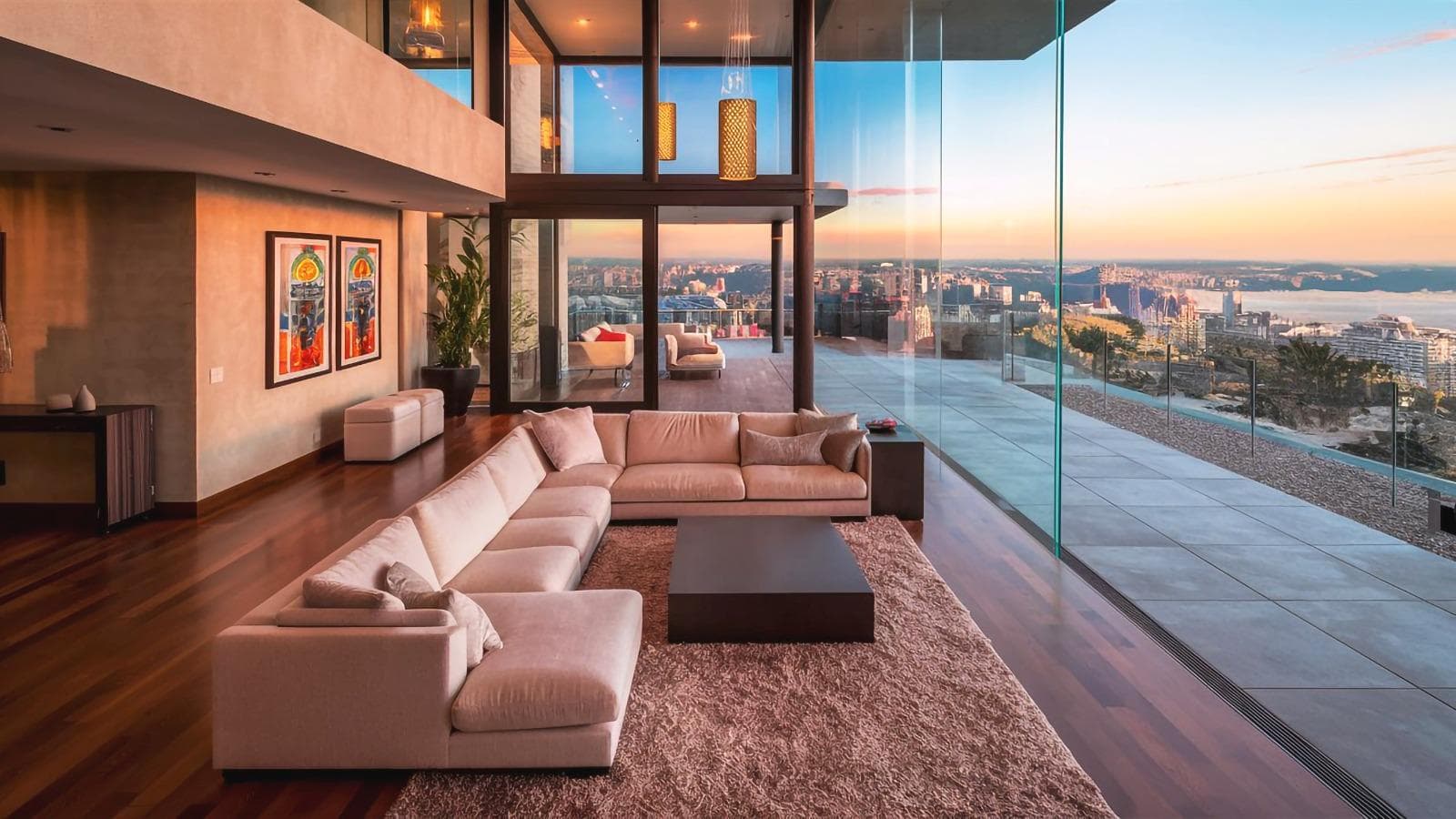 Open-plan penthouse living room with floor-to-ceiling glass and panoramic coastal city views at dusk